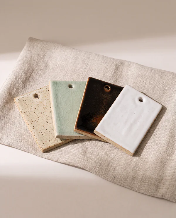 Four small ceramic glaze test tiles fanned out on natural linen
