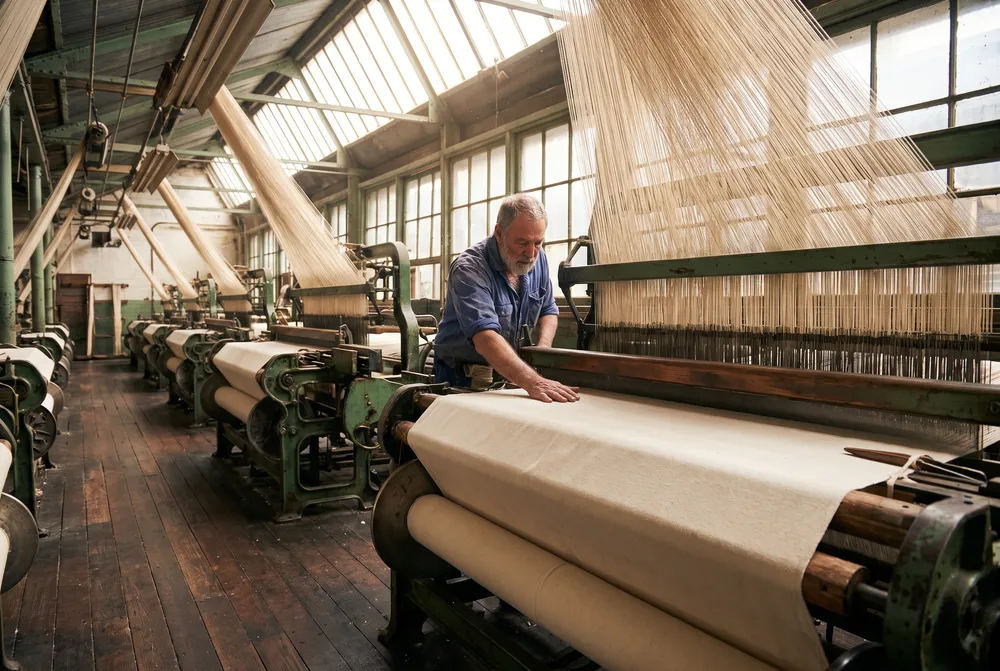 A weaver checking natural cotton duck on an old green loom in the Geelong mill