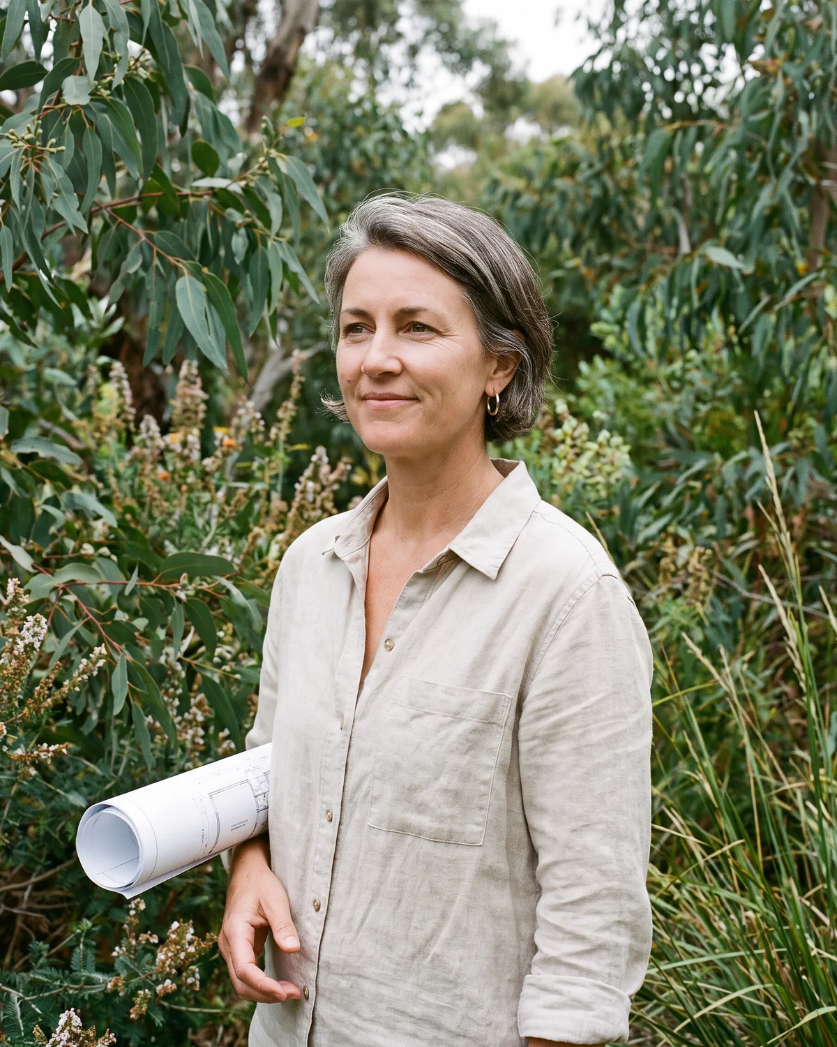 Ruth, the garden designer, holding a rolled planting plan in a native garden