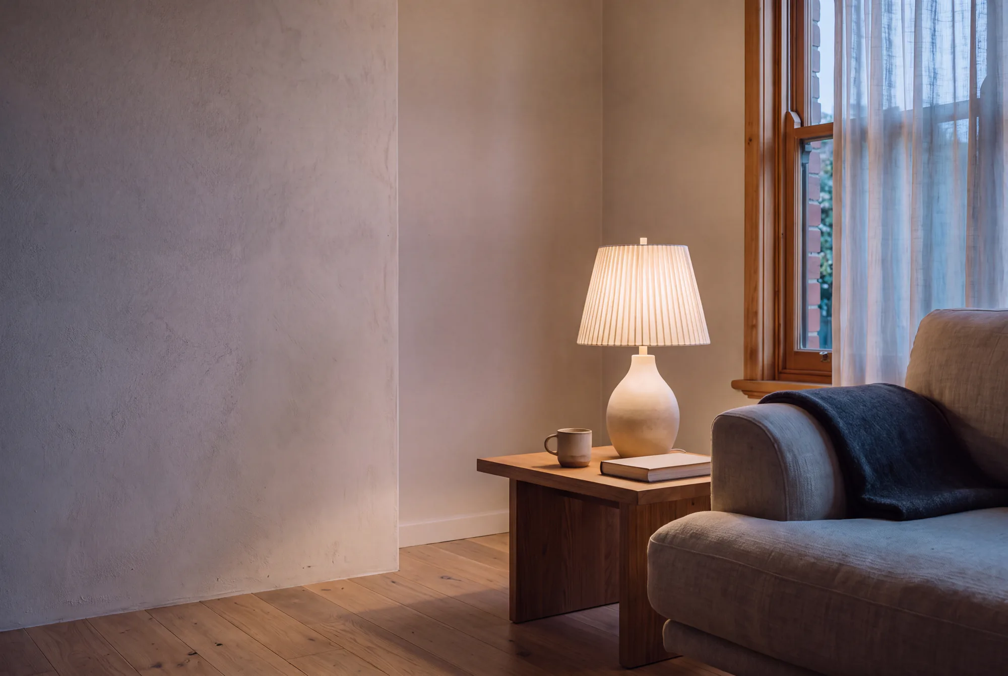 The same living room at dusk, with the speckled oat ceramic lamp switched on