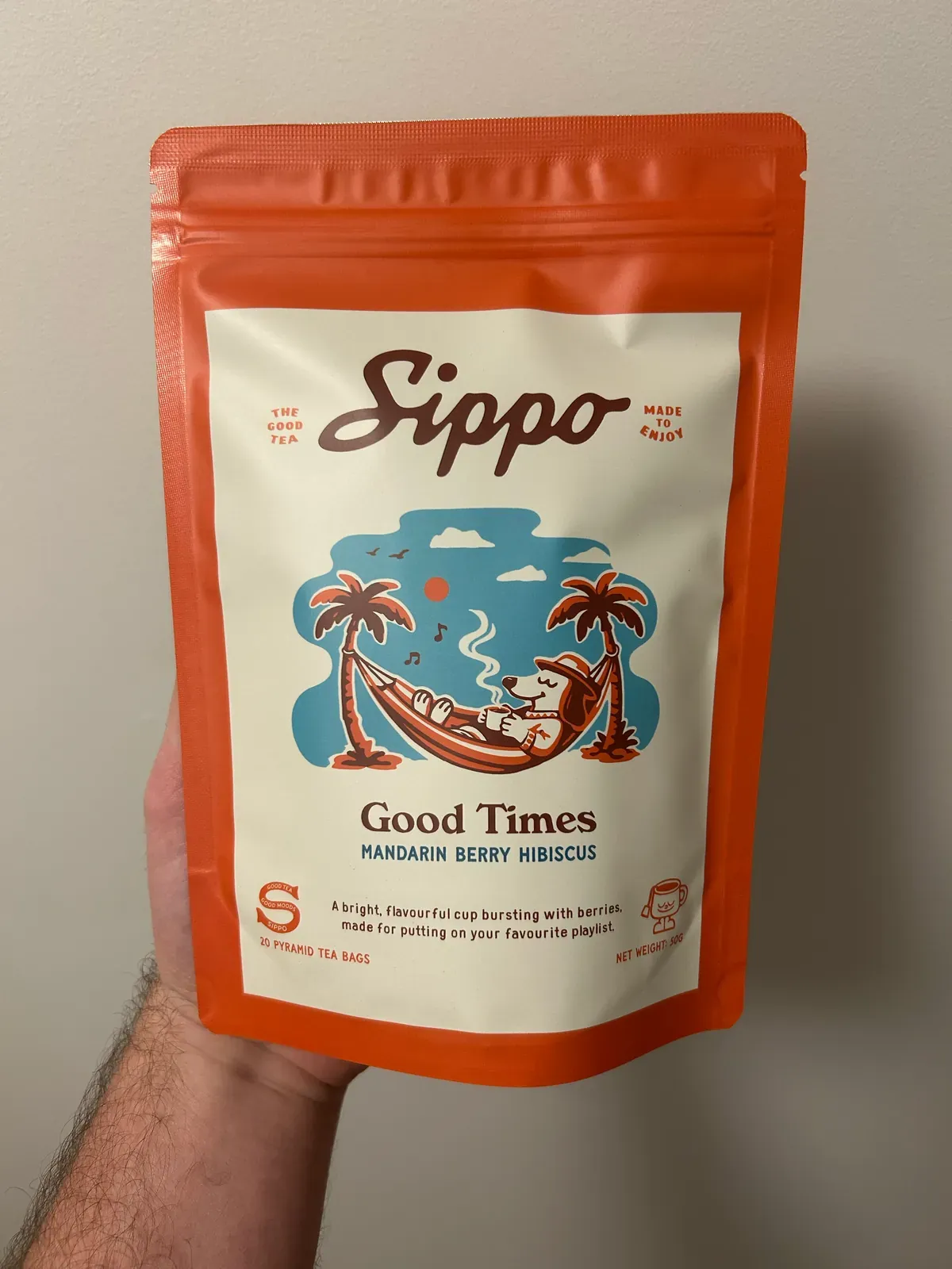 The same tea pack held up in front of a plain wall, photographed on a phone.